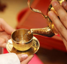 A person elegantly pours tea into a shimmering gold tea kettle, showcasing a moment of refined hospitality.